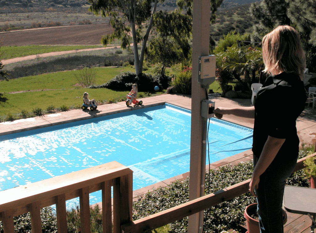 Automatic pool cover being operated while children play near the pool deck